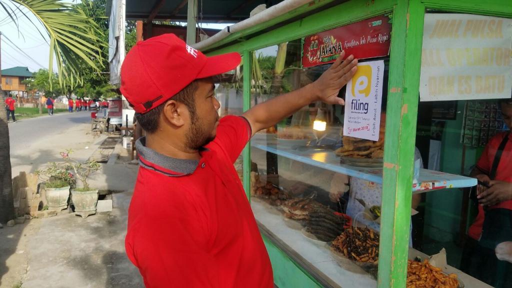Salah Satu Pegawai sedang Menempel Stiker e-filing pada Salah Satu Warung Makan